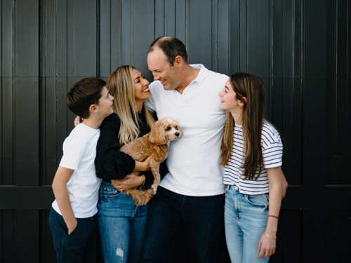Happy family standing outside in front of black garage door with pet dog - Australian Stock Image
