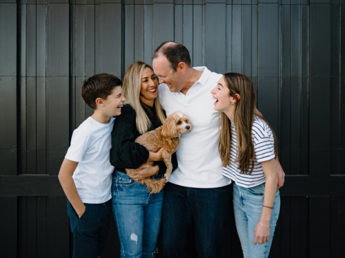 Happy family standing outside in front of black garage door with pet dog - Australian Stock Image