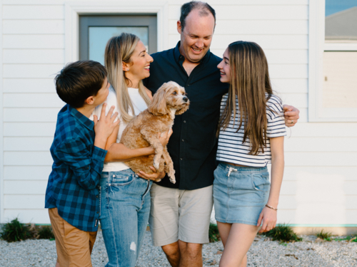 Happy family standing outside their home with their dog. - Australian Stock Image