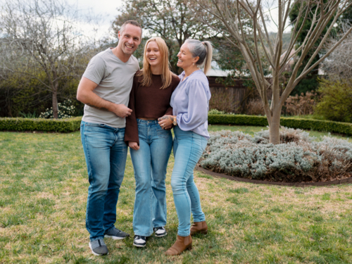 Happy family stands closely hugging each other in the garden of their new home - Australian Stock Image