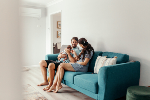 Happy family with newborn baby sitting on the lounge - Australian Stock Image