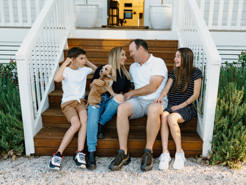 Happy family with their dog sitting on the steps of their home. - Australian Stock Image