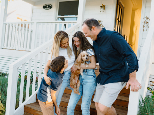 Happy family with their dog standing on the steps of their home. - Australian Stock Image