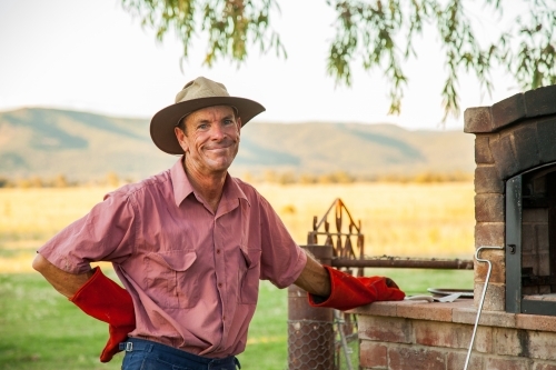 Happy farmer leaning on pizza oven at farm - Australian Stock Image