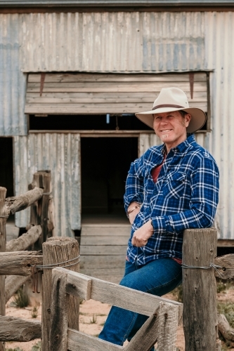 Happy farmer leans against sheep yards. - Australian Stock Image