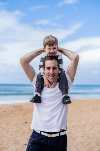 Happy father enjoys time with his young son at the beach under a clear blue sky - Australian Stock Image