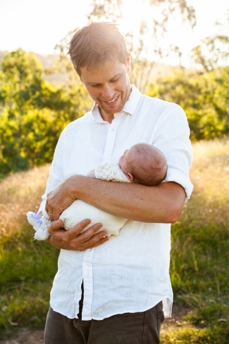 Happy father holding newborn baby girl in sunlight outside