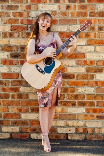 Happy female musician with guitar against brick wall