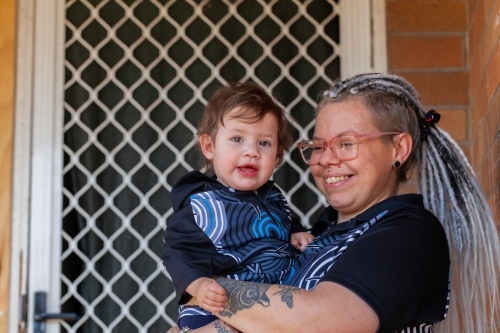 Happy First Nations Australian mum with baby girl by door of home - Australian Stock Image