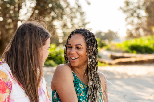 Happy First Nations Australian woman with teenaged daughter sitting together on a sand dune talking - Australian Stock Image