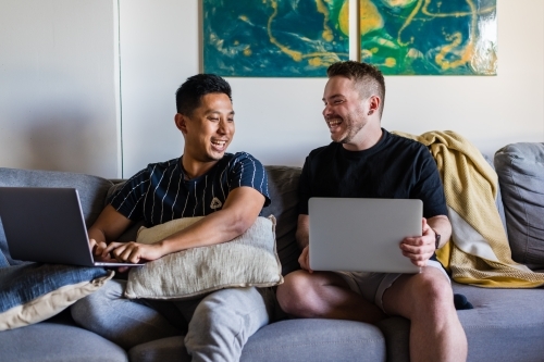 Happy gay couple at home, with laptops
