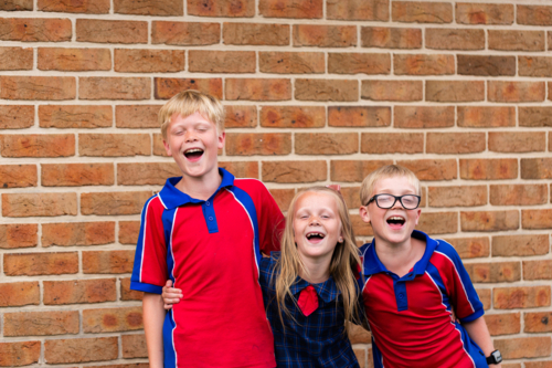 Happy group of three primary school kids laughing together with arms around each other - Australian Stock Image