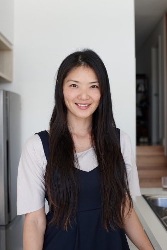 Happy Japanese woman standing in kitchen - Australian Stock Image