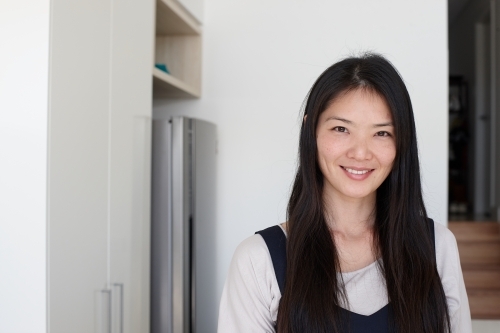 Happy Japanese woman standing in kitchen - Australian Stock Image