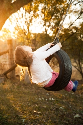 Happy kid playing in backyard on tyre swing - Australian Stock Image