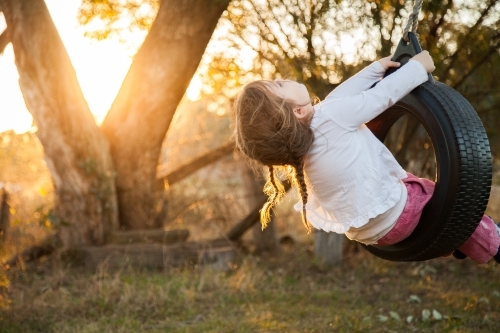 Happy kid playing in backyard on tyre swing - Australian Stock Image