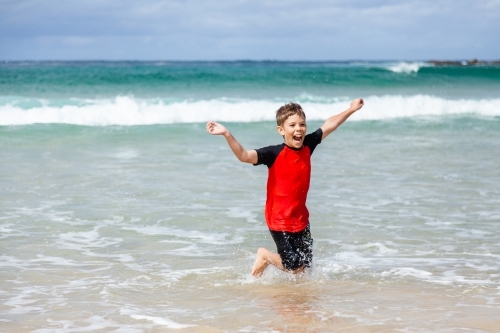 Happy kid running and splashing in seaside waves at the beach - Australian Stock Image