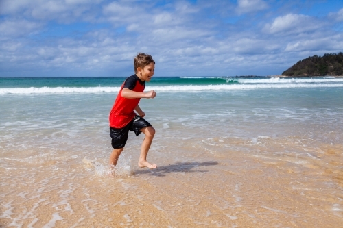 Happy kid running and splashing in seaside waves at the beach - Australian Stock Image