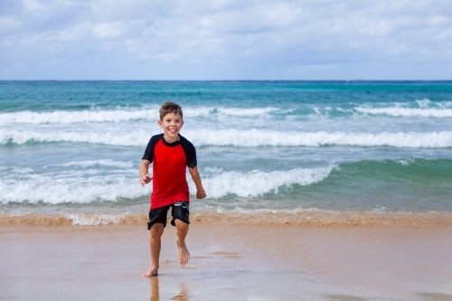 Happy kid running and splashing in seaside waves at the beach - Australian Stock Image
