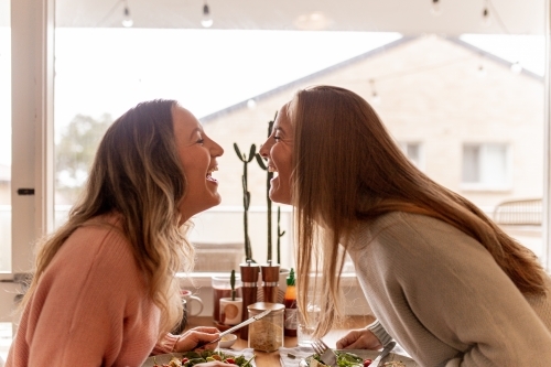 Happy, laughing female same sex couple at the dining table with their faces close to one other