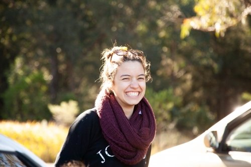 Happy laughing young woman wearing scarf in winter beside car - Australian Stock Image