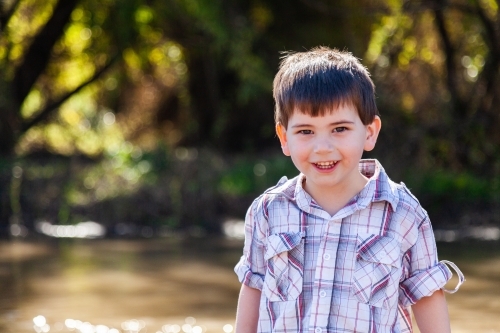 Happy little boy smiling beside river - Australian Stock Image