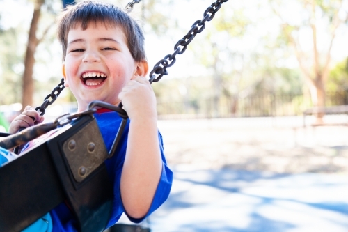 Image of Happy little boy swinging on a swing at the park