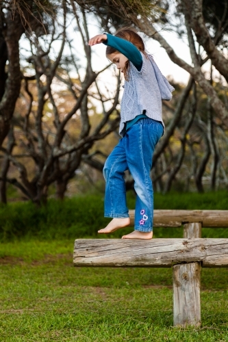 Happy little girl balancing on a pole outside near forest