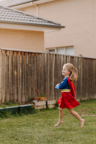 Happy little girl in a superhero costume running around backyard - Australian Stock Image