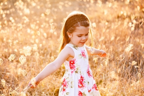 Happy little girl laughing and spinning in sunlit grass - Australian Stock Image