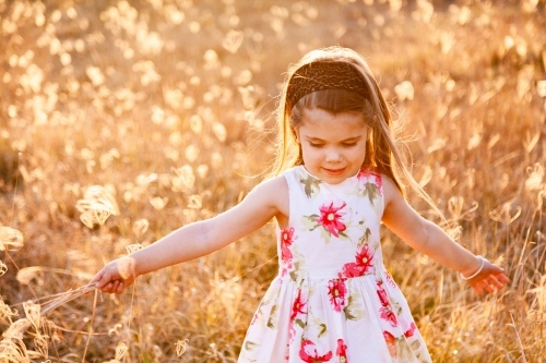 Happy little girl laughing and spinning in sunlit grass - Australian Stock Image