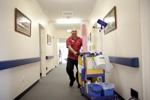 Happy male nursing home cleaner doing rounds - Australian Stock Image
