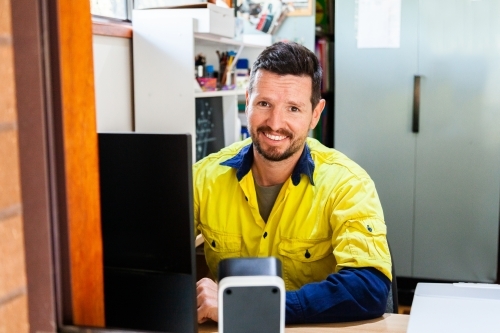 Happy male tradie at computer in home office - Australian Stock Image