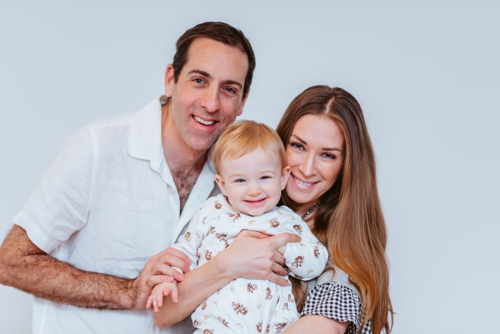 happy mid aged family of mid aged female mom and male dad holds up a young baby boy with blond hair - Australian Stock Image