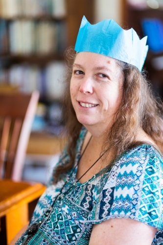 Happy middle aged woman smiling at Christmas wearing blue paper crown - Australian Stock Image