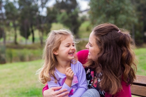 Happy mother and daughter laughing and giggling together outside at park - Australian Stock Image