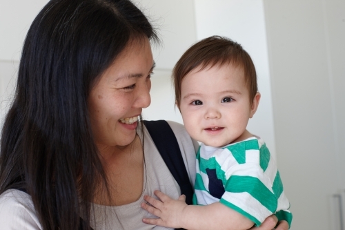 Happy mother holding baby boy in kitchen - Australian Stock Image