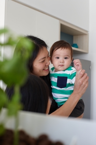 Happy mother holding baby boy in kitchen - Australian Stock Image