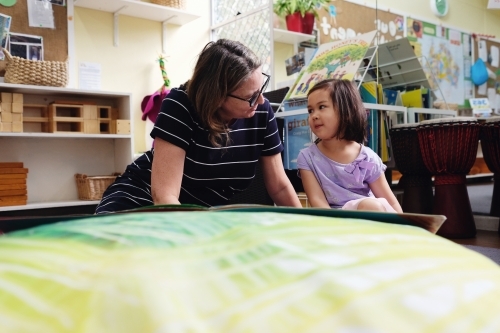 Happy multicultural teacher and child reading a book in kindergarten - Australian Stock Image