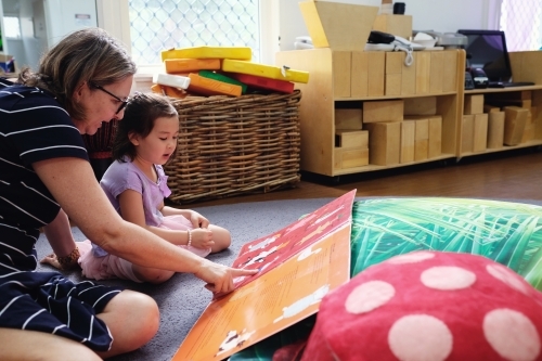 Happy multicultural teacher and child reading a book in kindergarten