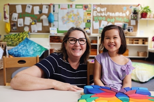 Happy multicultural teacher and child with wooden blocks puzzles in kindergarten - Australian Stock Image