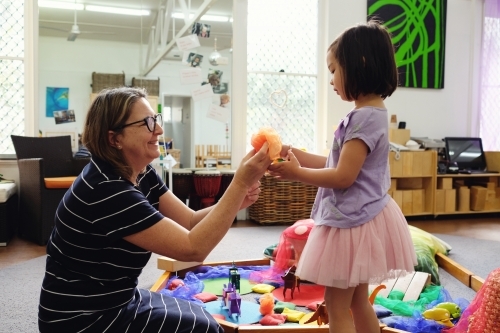 Happy multicultural teacher and child with wooden blocks puzzles in kindergarten - Australian Stock Image