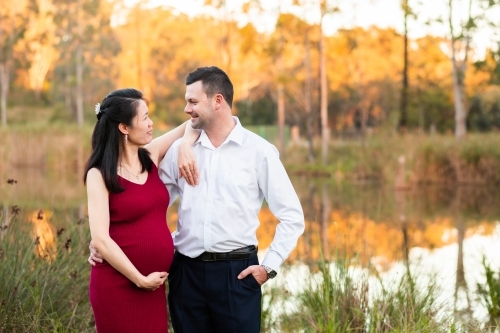 Happy pregnant couple standing together by dam in country Asian woman and Caucasian man