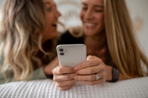 Happy same sex couple lying on a bed looking at a smart phone - Australian Stock Image