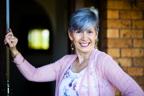 happy senior woman standing at her front door to welcome visitors