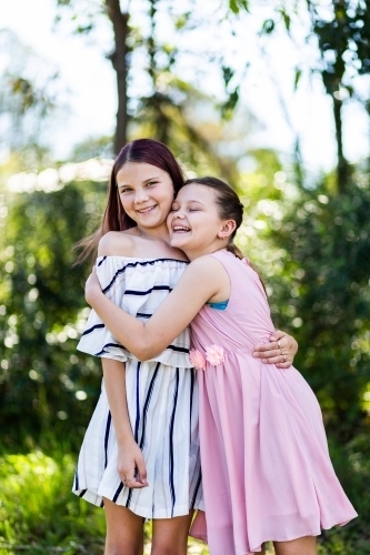 Happy sisters in party dresses hug outside