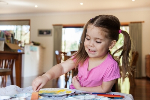 Happy smiling girl painting a picture in pre-school - Australian Stock Image