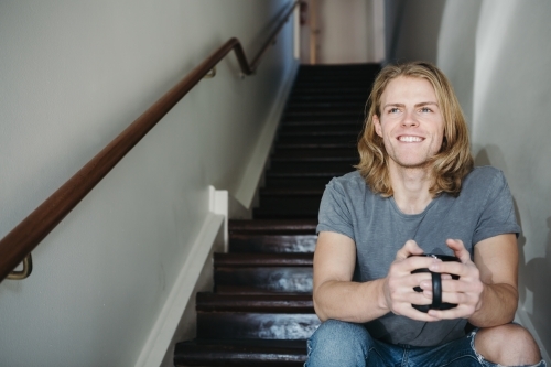 Happy smiling guy sitting on stairs with a coffee mug