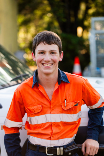 happy smiling portrait of young male trade apprentice person in high-vis workwear beside vehicle - Australian Stock Image