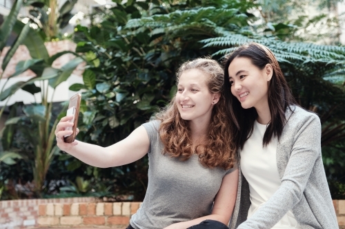 Happy students girl friends using mobile - Australian Stock Image